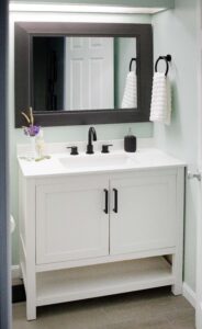 small bathroom with pale green walls with white cabinets