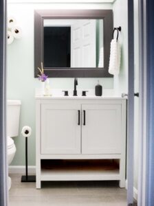 small bathroom with pale green walls with white cabinets