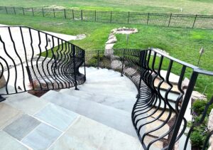 large stone stairs with an iron railing leading down to a backyard