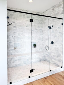 large glass shower with mottled white and black tiling and black faucets